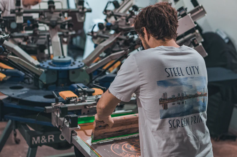 Printer running a multi-station screen printing press loaded with black t-shirts